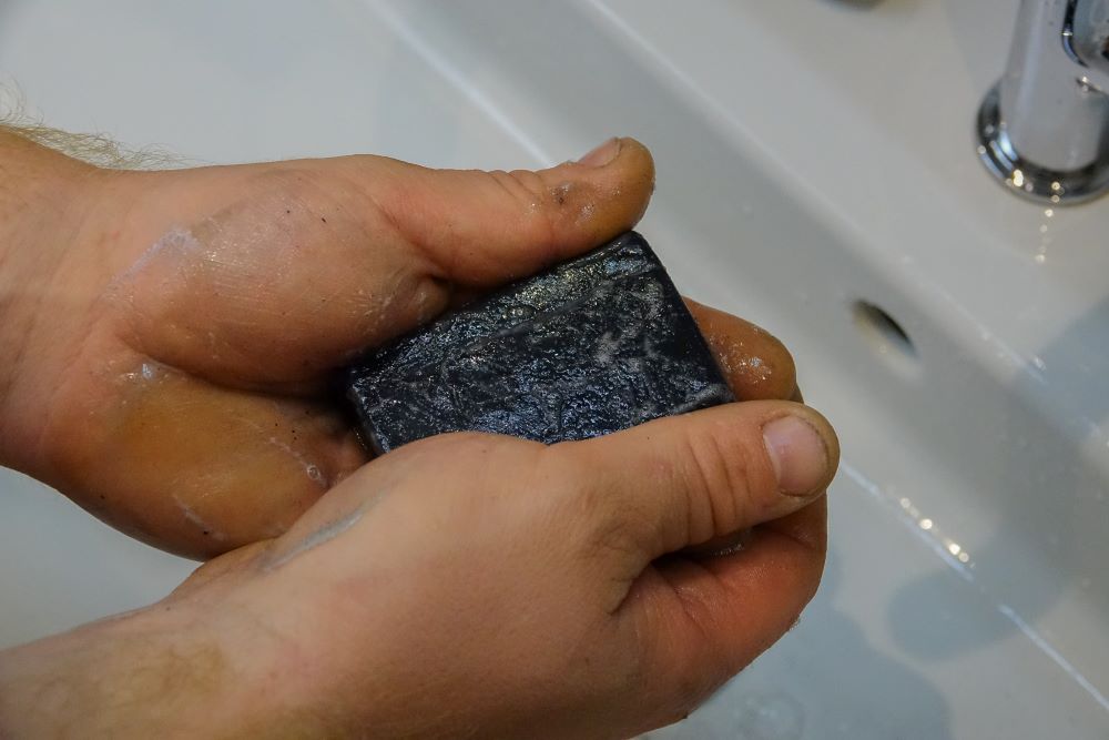 Dreckige Arbeiterhände werden mit der schwarze Kohleseife im Waschbecken gewaschen.