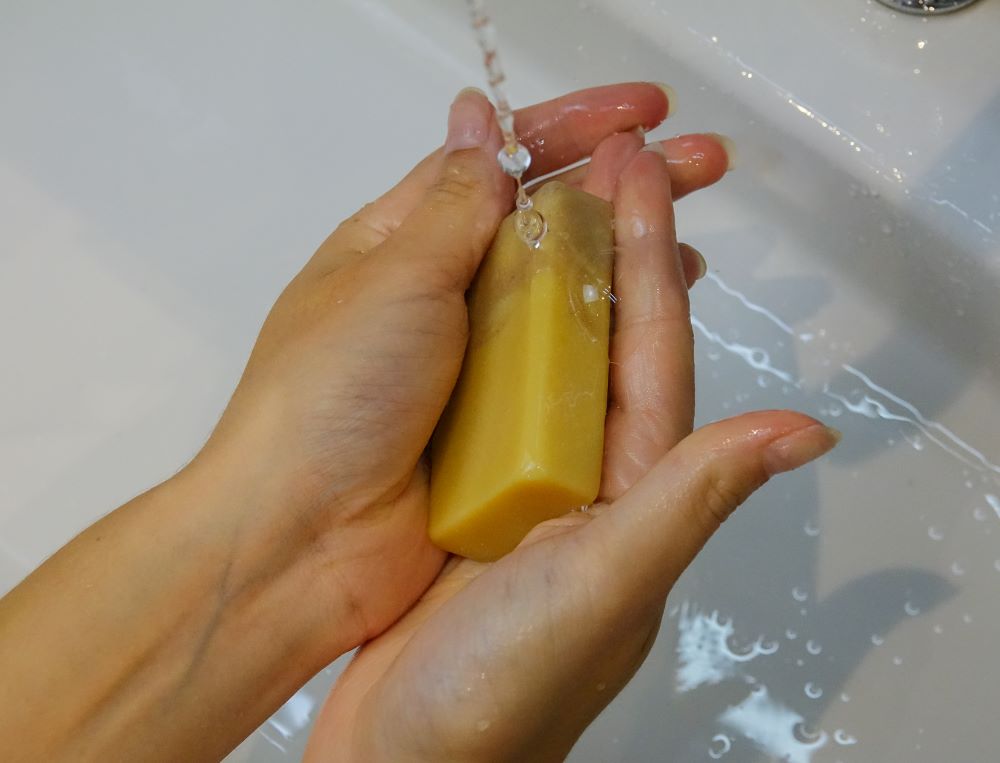 Die Hände werden mit der Cremig zur Haut Ziegenmilchseife unter dem Wasserhahn gewaschen.
